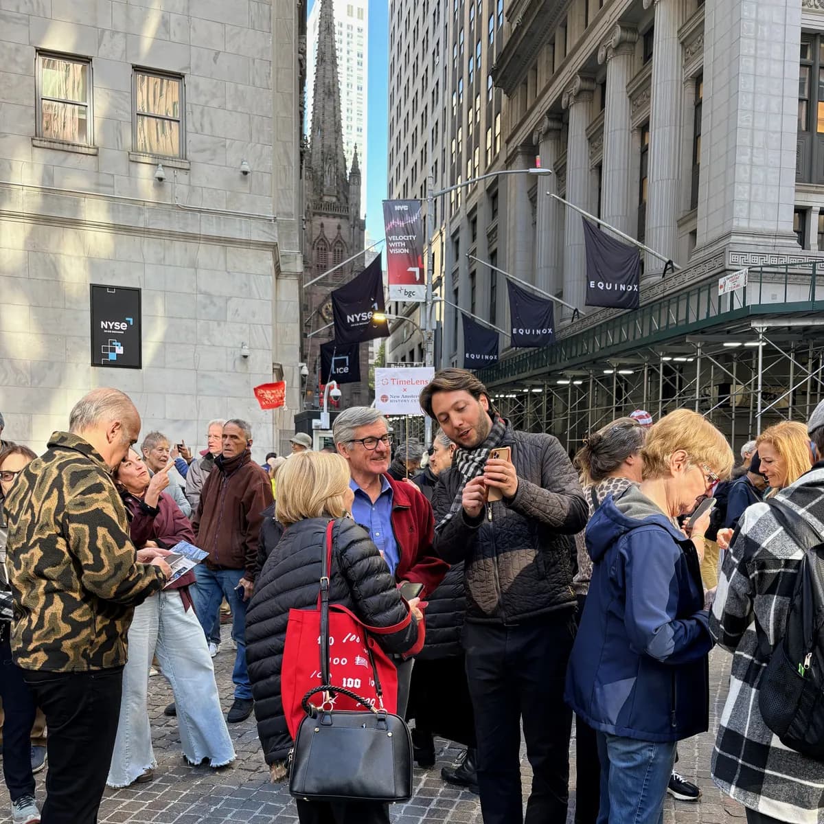 Gruppe mit Smartphones an der Wall Street neben der New York Stock Exchange, mit einem Schild von TimeLens x New Amsterdam History Center